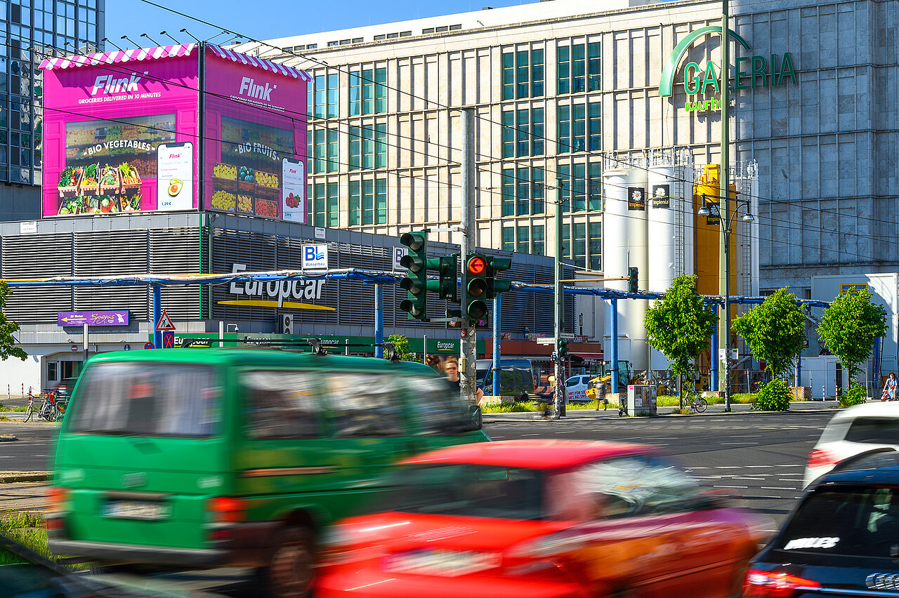 Das auffällige Riesenposter von Flink über dem Europcar-Gebäude bewirbt Bio-Lebensmittel und schnellen Lieferservice in leuchtendem Pink.