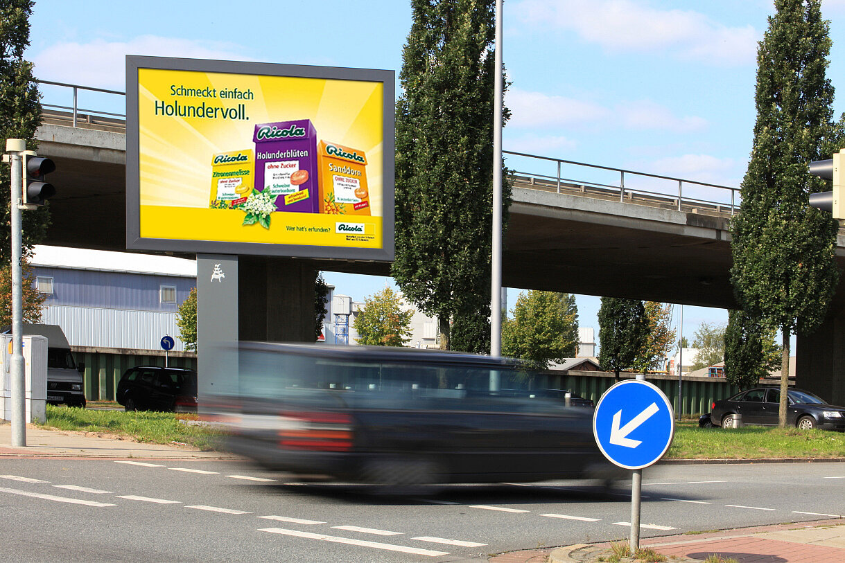 Mega-Light auf Sockel steht imposant an Verkehrsstraße mit Motiv von Ricola