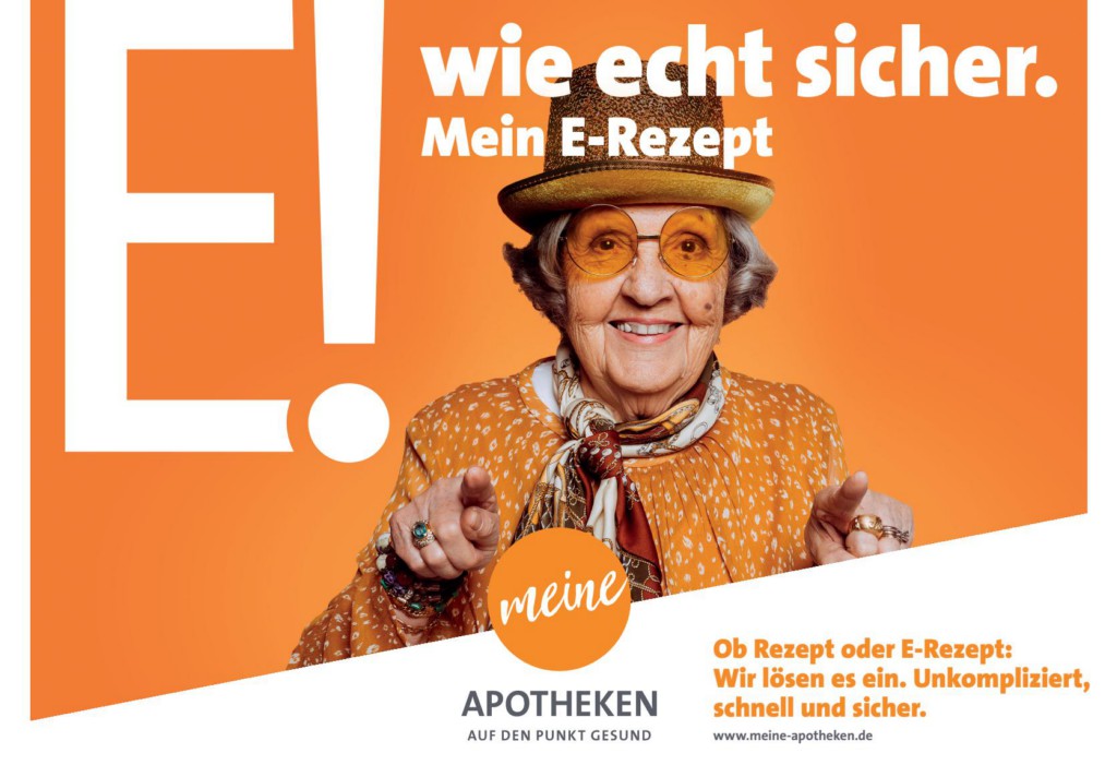 Plakatmotiv: Ältere Frau mit Hut und bunter Kleidung lächelt und zeigt auf den Betrachter. Im Hintergrund der Slogan 'E! wie echt sicher. Mein E-Rezept'. Werbung für sicheres Einlösen von E-Rezepten bei 'meine Apotheken'.