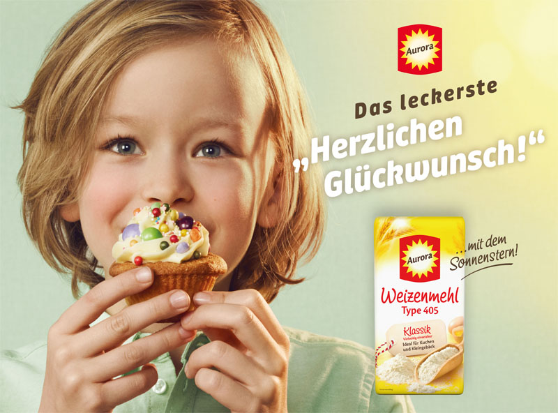 Plakatmotiv von Aurora mit einem Kind, das einen Muffin isst, und der Botschaft „Das leckerste Herzlichen Glückwunsch“ – Werbung für Weizenmehl.