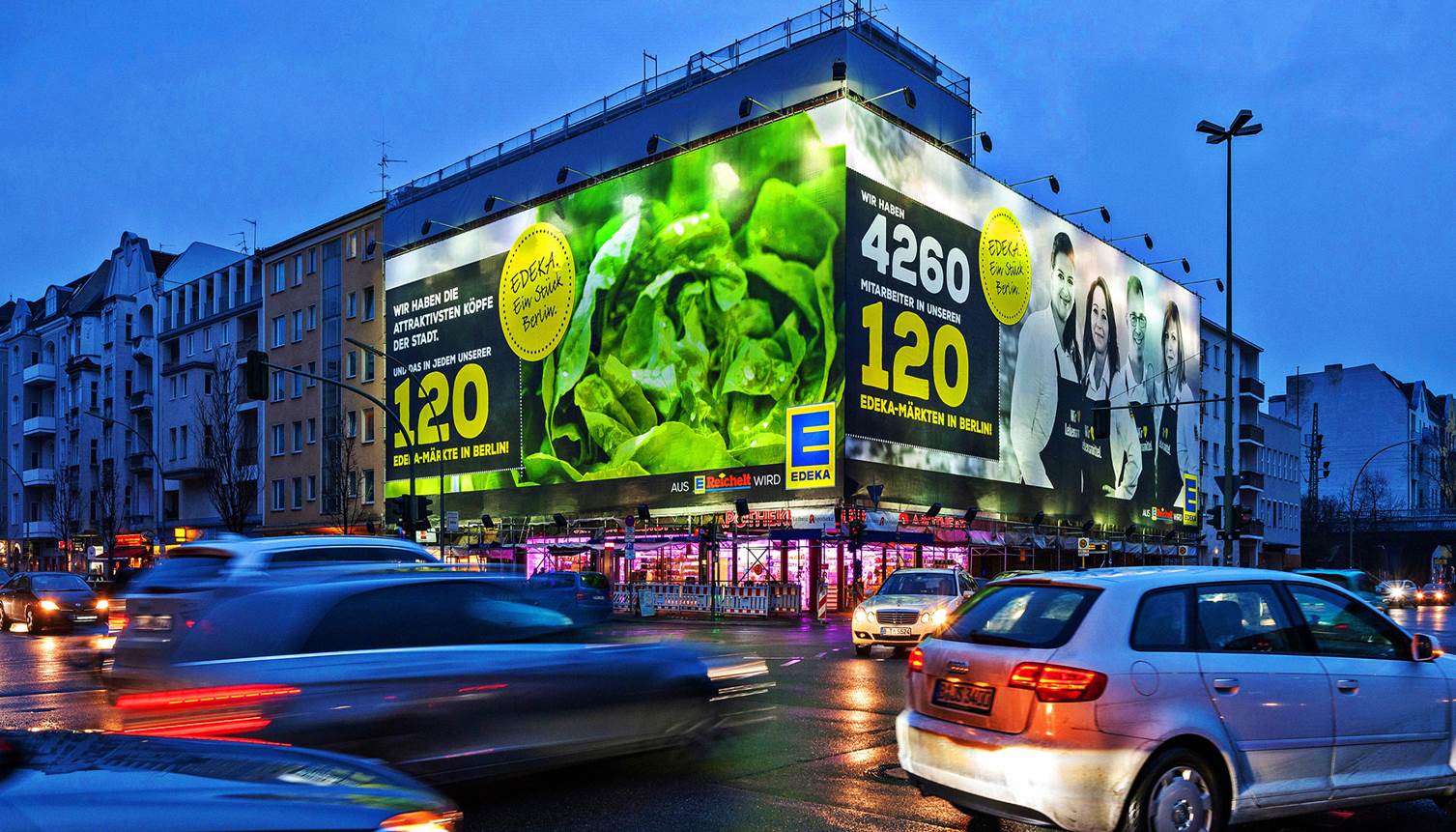 Ein leuchtend beleuchtetes XXL-Poster von EDEKA zeigt Salat und Mitarbeitende